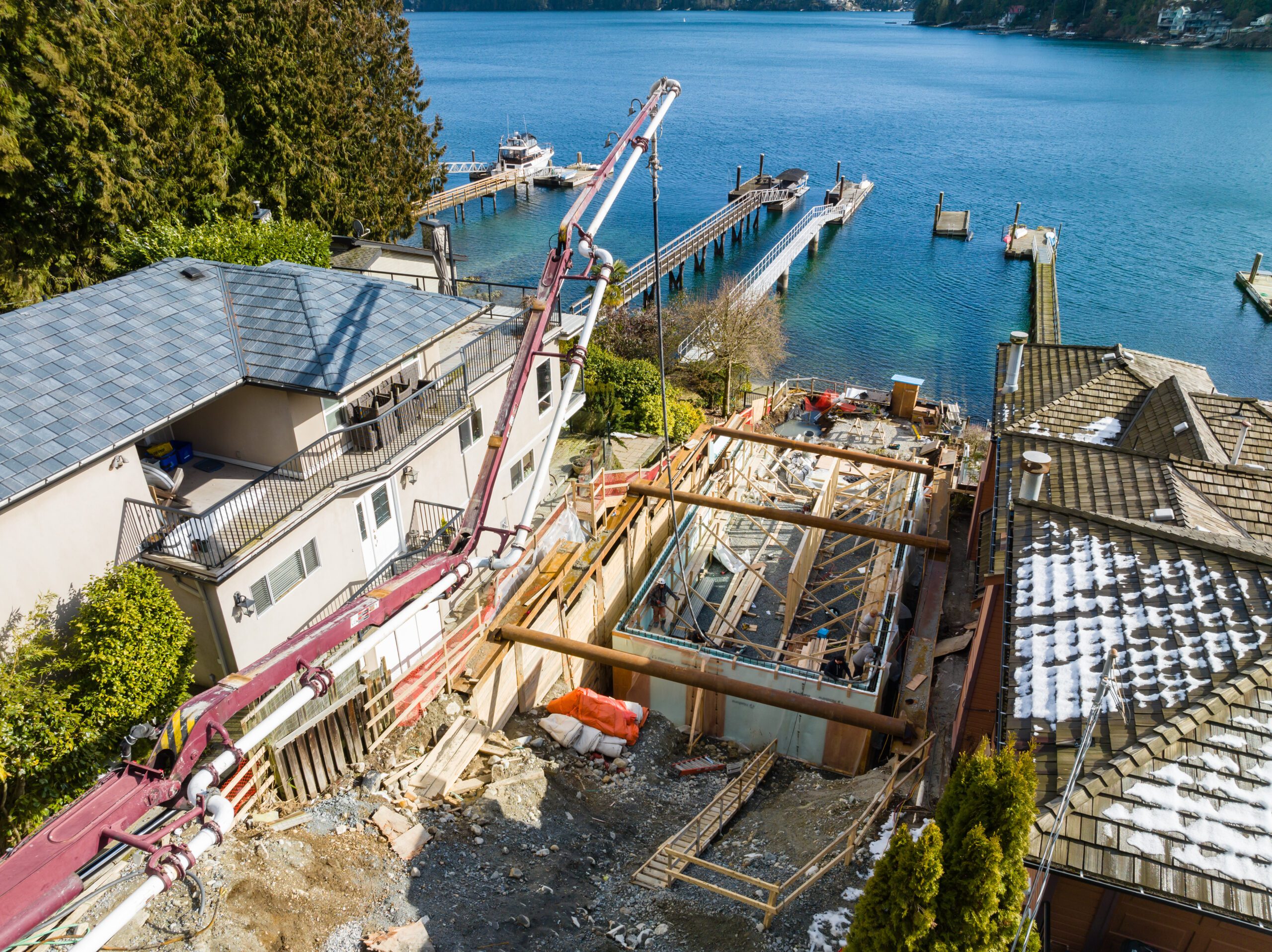 Concrete pump extending over the Fala custom home foundation during construction on a steep lot in Deep Cove.