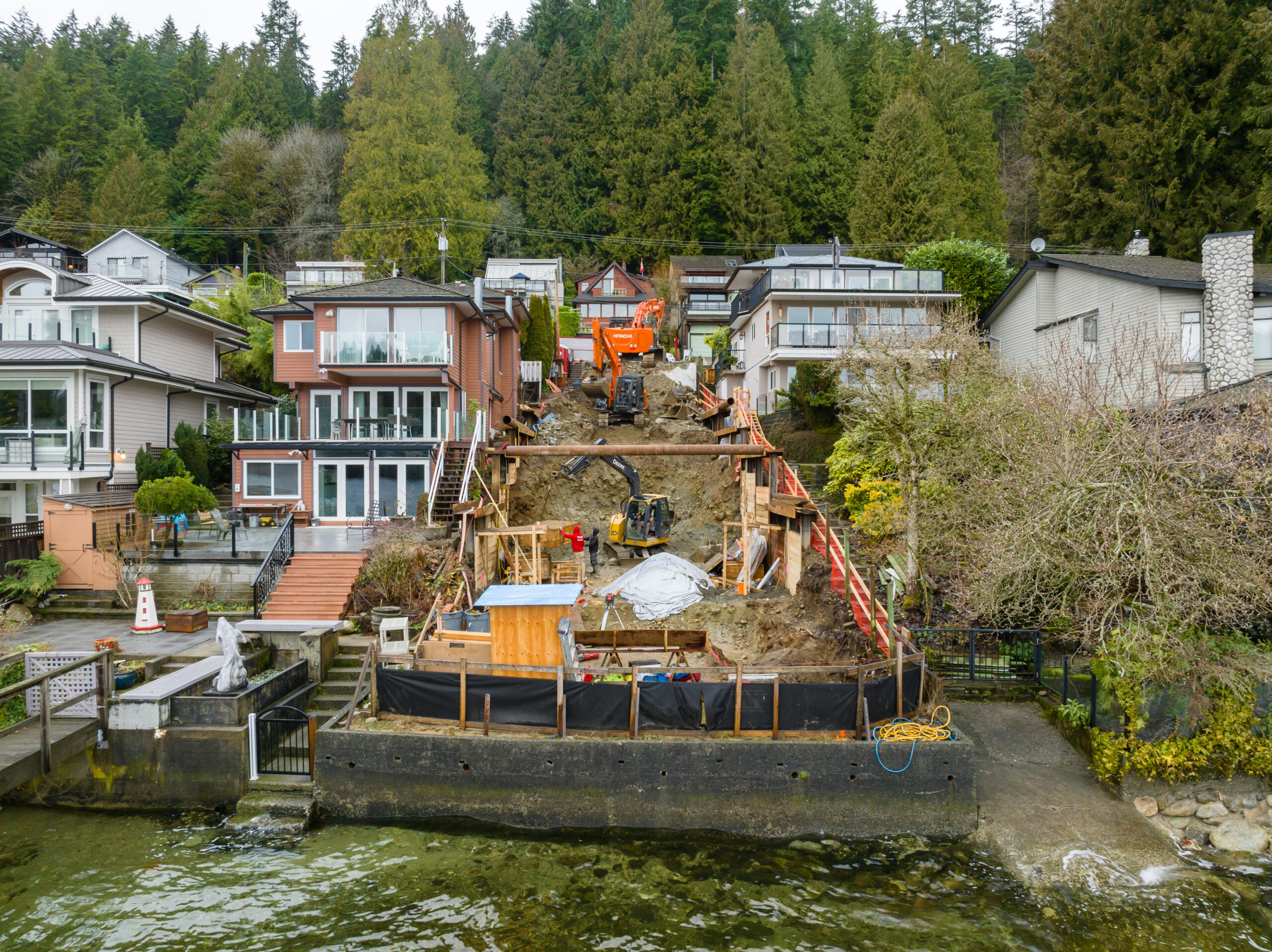 Building a house on a steep slope in North Vancouver, showing excavation and temporary supports at the Fala waterfront project.