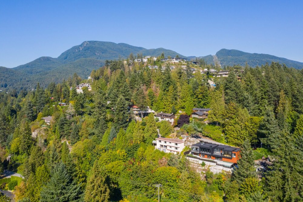 Aerial view of a modern Hasler Homes custom home surrounded by forested hillsides in North Vancouver.